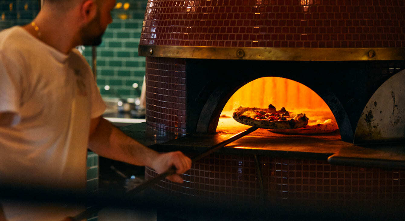 Pizzabäcker schiebt eine neapolitanische Pizza in den befeuerten Kuppelofen des Spezzagrano